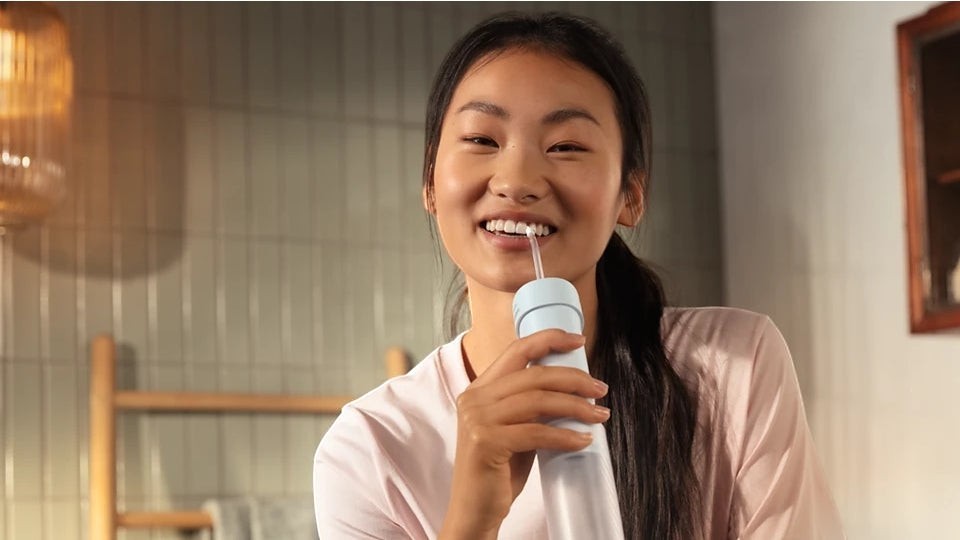 Taghareed Philips Sonicare compact water flosser with 3 modes and 360° rotating nozzle being used by a smiling young woman.