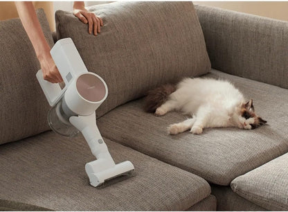 Person using a handheld vacuum cleaner on a brown sofa with a cat lying on it.