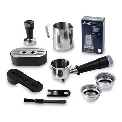 A coffee brewing accessory set arranged on a white background, including a stainless steel milk pitcher, portafilter with black handle, tamper, espresso filter basket, cleaning brush, lid tool, two metal filter baskets, and a dark blue retail box. The box shows the Delonghi brand.