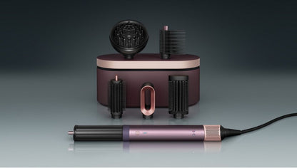 A hair styling tool set with a metallic purple and rose gold cylindrical wand, several black brush attachments, and a matching charging case on a dark gray gradient background.
