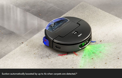 A black robotic vacuum cleaner with blue and green illuminated accents is shown on a light carpet in a real indoor environment, with debris being lifted and a green light beam projected. Text at the bottom states suction is boosted up to 4x when carpets are detected.
