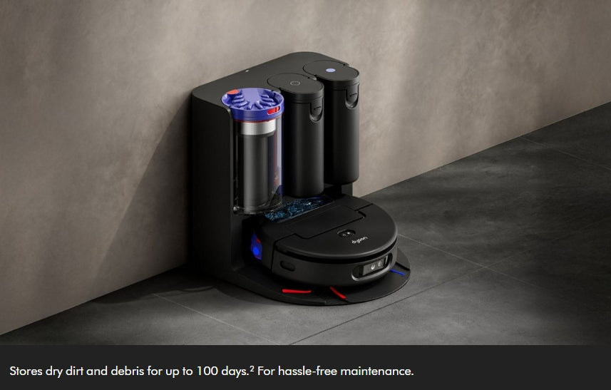 A black robotic vacuum cleaner docked at a matching black charging and cleaning station against a textured gray wall and dark floor. The station includes a transparent dust container with blue lighting accents.