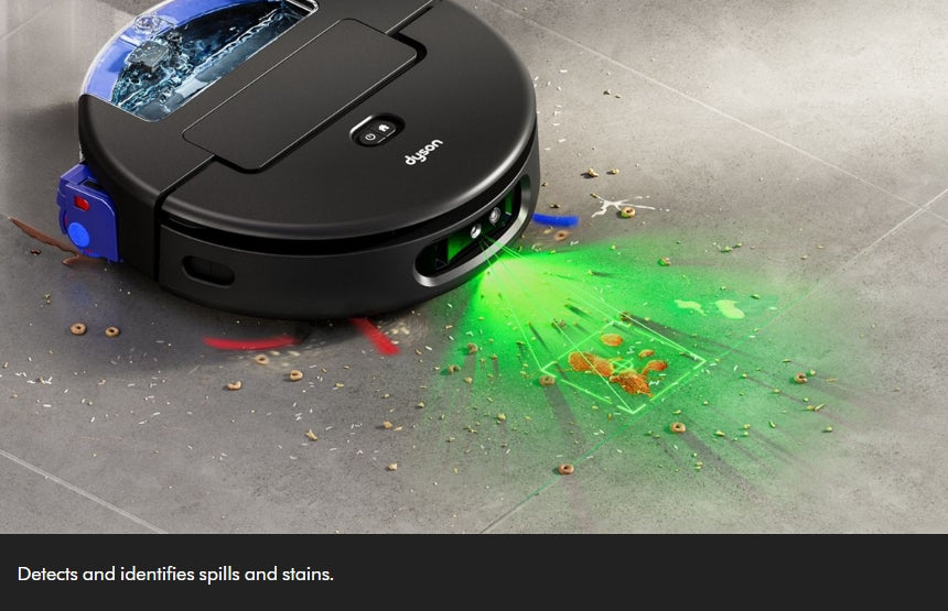 A Dyson robotic vacuum cleaner shown on a gray tiled floor, with a bright green light projected onto spilled liquids and debris to demonstrate spill and stain detection.