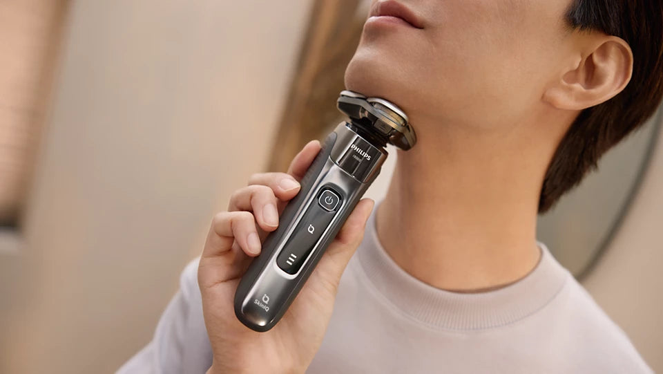 Person using a electric shaver on their neck with a neutral background