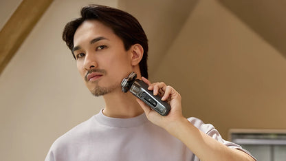 Man using an electric shaver in a neutral indoor setting