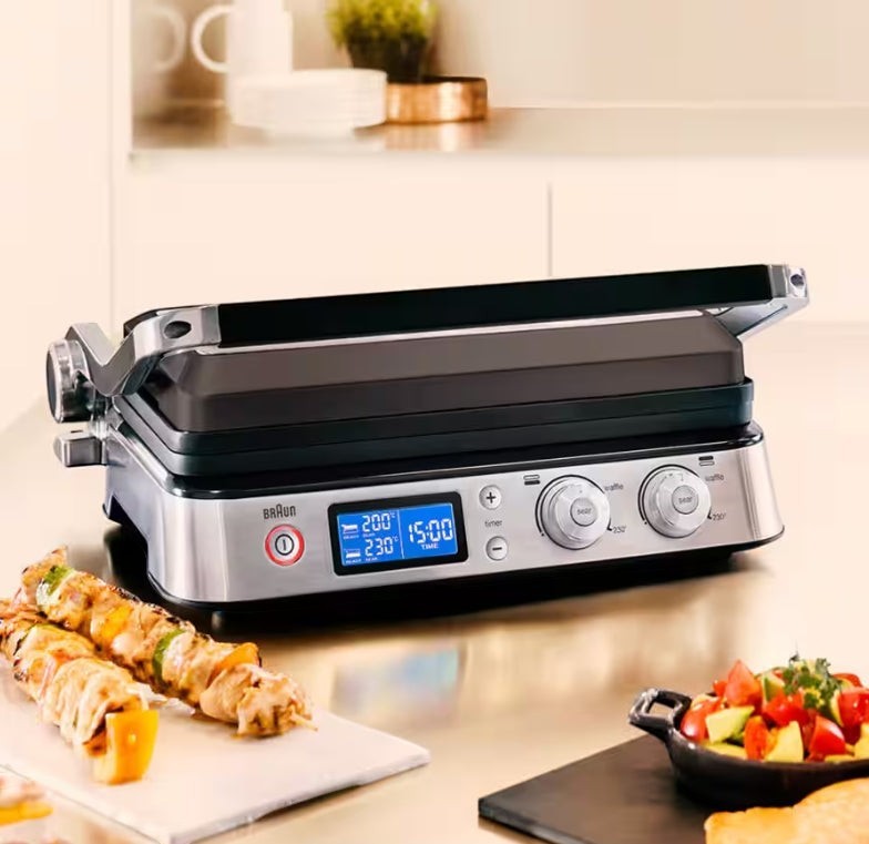Taghareed Braun MultiGrill 9 CG9040 stainless steel electric contact grill with digital display and adjustable knobs, shown with skewers of food.