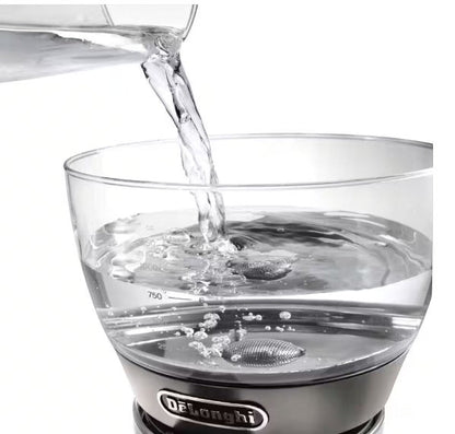 Taghareed De'Longhi Clessidra filter coffee maker, clear glass water tank with measurement markings, water being poured in.