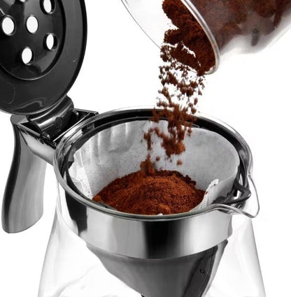 Taghareed De'Longhi ICM17210 filter coffee maker, adding ground coffee to paper filter. Glass carafe with stainless steel accents.