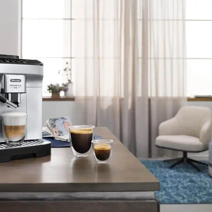 Taghareed De'Longhi Magnifica Evo automatic coffee machine in silver and black, brewing a latte. Two espresso cups are on the counter.