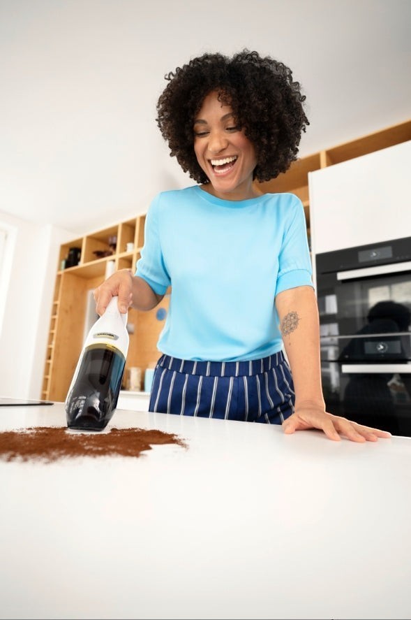 Taghareed Kärcher CVH 2 battery-powered hand vacuum cleaner with HEPA filter cleaning coffee grounds from a white countertop.