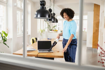 Taghareed Kärcher CVH 2 cordless handheld vacuum cleaner with HEPA filter, white and black, cleaning a laptop.