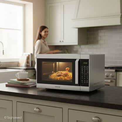 Taghareed Kenwood 42L digital microwave with grill, 1100W, stainless steel, featuring a digital display and cooking food inside.