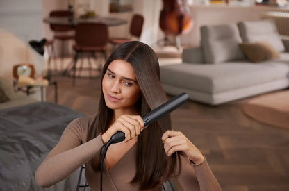 Taghareed woman straightening her long brown hair with a black Philips 5000 Series straightener featuring argan-oil-infused plates.