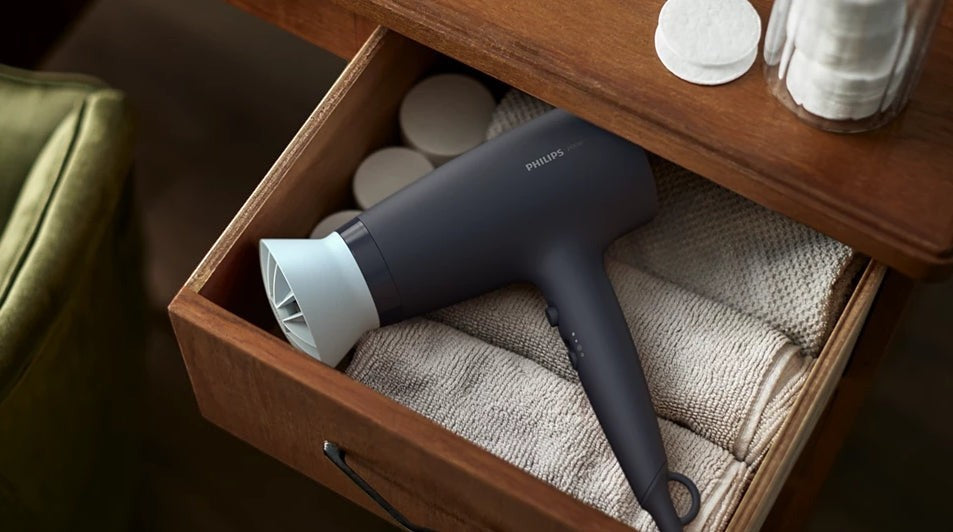 Taghareed Philips 3000 Series dark grey hair dryer with white nozzle, stored in a drawer with towels.