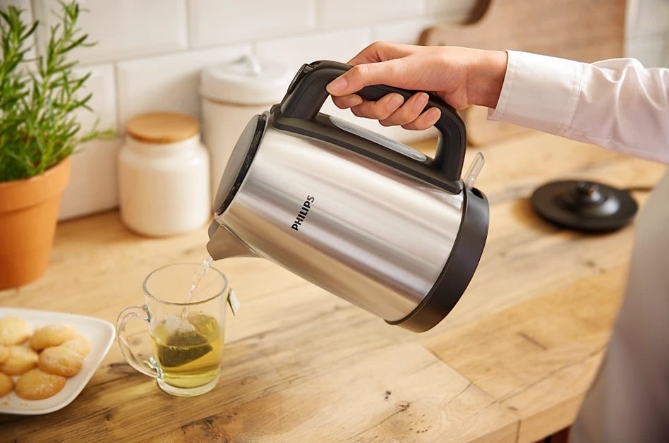 Taghareed Philips stainless steel kettle pouring hot water into a glass mug with a tea bag.